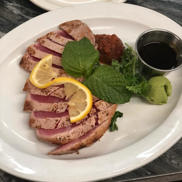 Seared tuna slices with lemon, mint, wasabi, and sauces on a white plate.