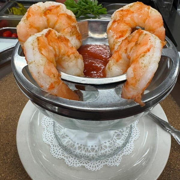 Four large shrimp cocktail with red sauce and parsley in a metal and glass serving dish.