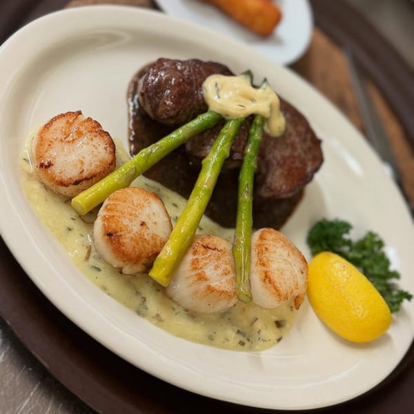 Coach & Four's steak and scallops with asparagus, sauce, and a lemon wedge on a white plate.